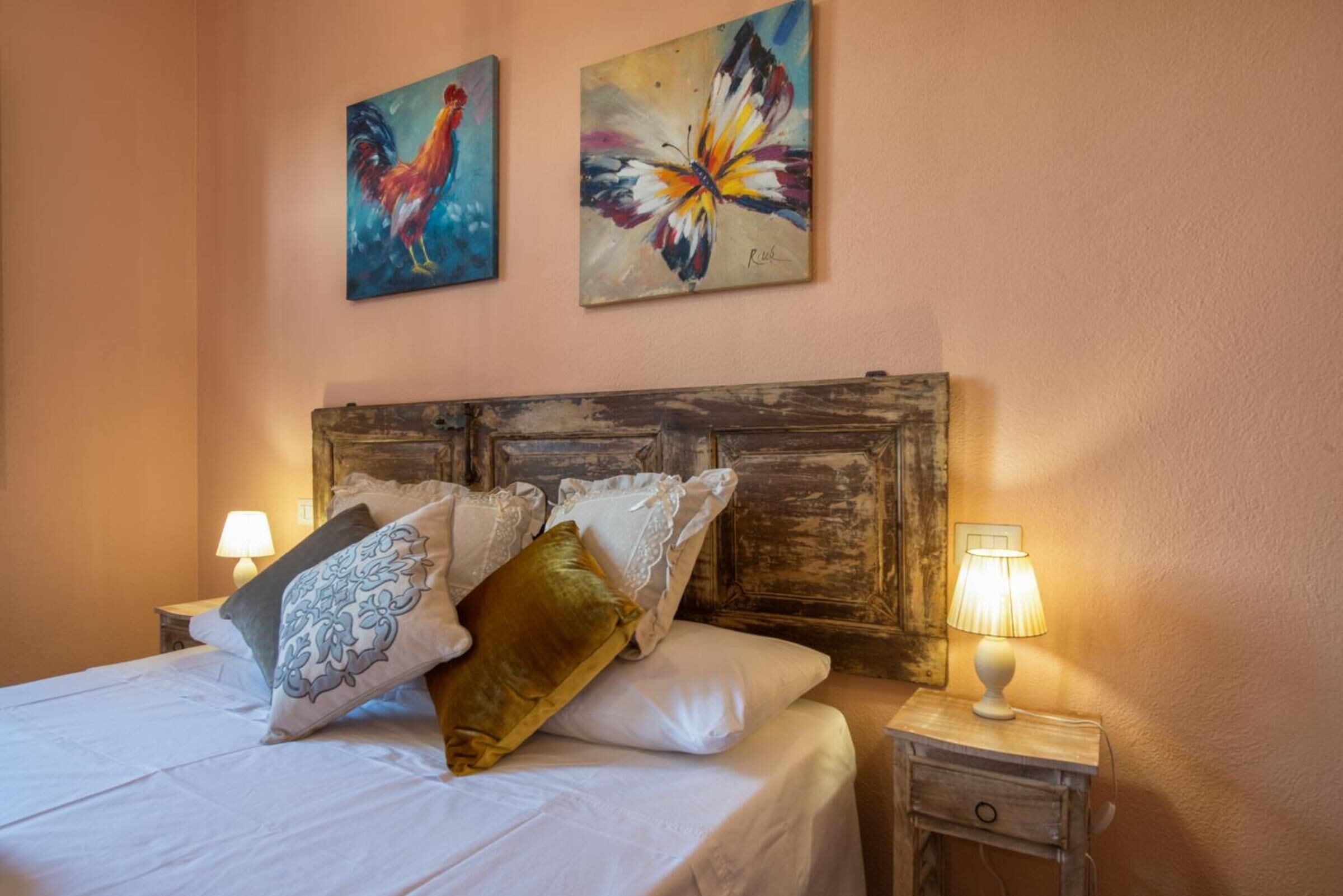 A bedroom with a wooden headboard, a bed with white linens and decorative pillows, two wall-mounted paintings, and bedside lamps.