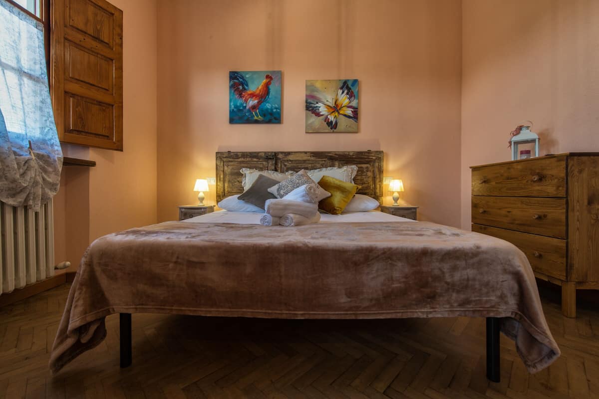 Un dormitorio con una cama grande, cabecera de madera, dos cuadros, lámparas de noche y un aparador de madera.