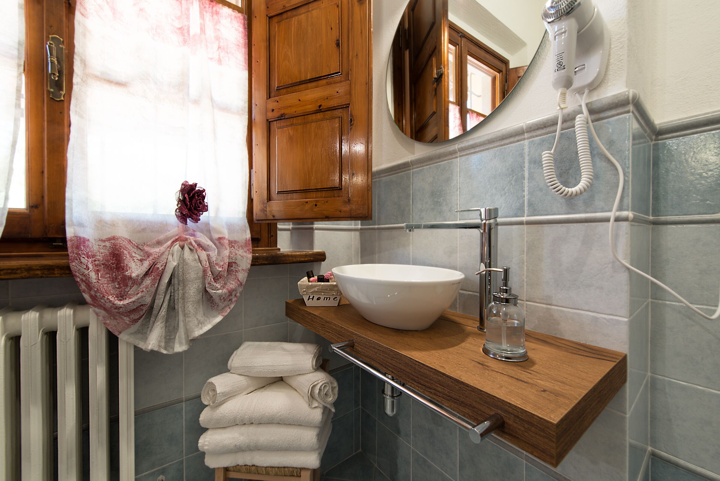 A bathroom with a wooden vanity, a white sink, a hairdryer, and a towel rack with folded towels.