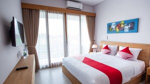 Une chambre d’hôtel avec un grand lit, une télévision, un bureau et une fenêtre avec des rideaux.
