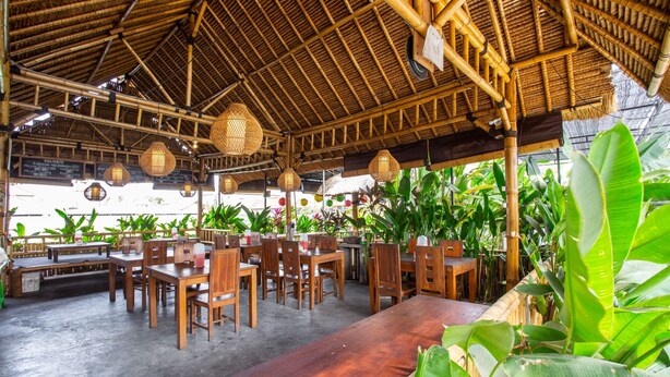 Un restaurant doté de plafonds en bambou, de tables et de chaises en bois, et entouré d’une végétation luxuriante.