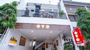 Un bâtiment moderne, avec une enseigne « OYO » bien visible à l’entrée, un escalier menant à l’étage supérieur et un balcon agrémenté de plantes.