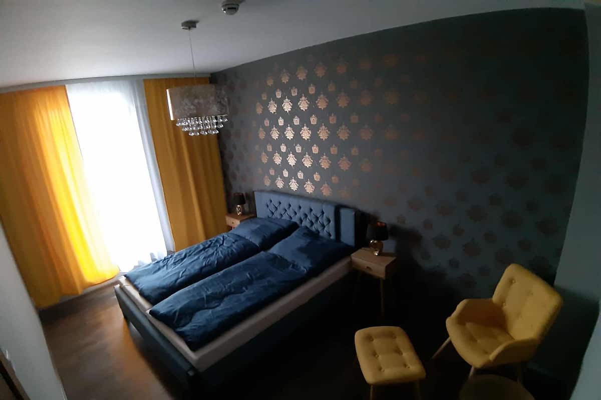 A bedroom with a bed, two bedside tables, a chandelier, and two chairs.