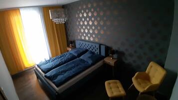 Un dormitorio con una cama, dos mesitas de noche, una araña y dos sillas.