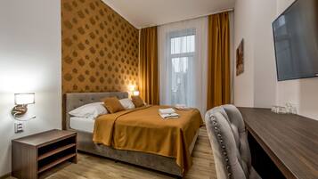 Una habitación de hotel con cama, mesita de noche, televisor y ventana con cortinas.