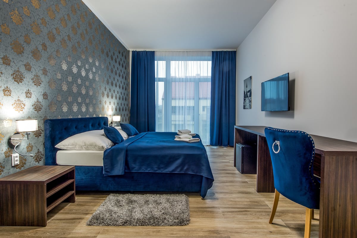 A bedroom with a bed, bedside tables, a desk, a chair, and a TV on the wall.
