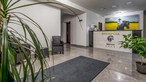 A reception area with a marble floor, a reception desk with a horse logo, and a painting of a horse and rider. - Black Horse (Prešov)