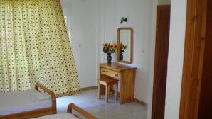 A bedroom with two wooden beds, a wooden dresser, a mirror, and a window with a patterned curtain. - Mejanis (Corfu)