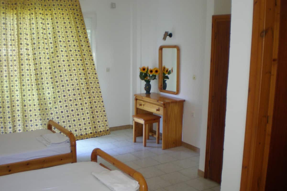 A bedroom with two wooden beds, a wooden dresser, a mirror, and a window with a patterned curtain.