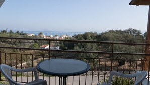 A balcony with a table and chairs, overlooking a coastal town with houses and trees. - Mejanis (Corfu)