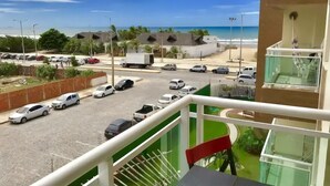 Blick vom Balkon auf eine Straße mit parkenden Autos, einen Strand und einen klaren Himmel.