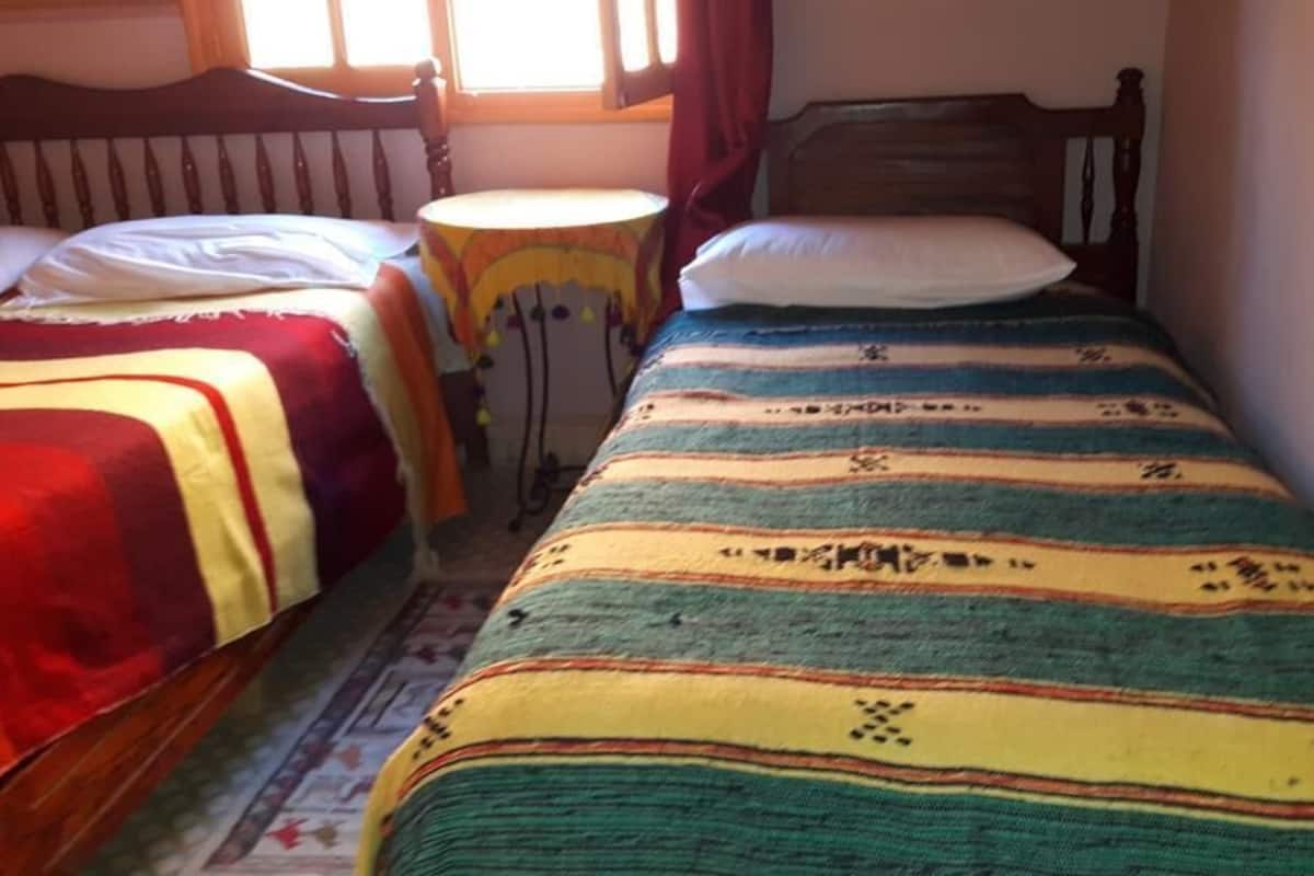 Une chambre avec deux lits, chacun recouvert d’une couvre-lit à motifs. Une petite table ronde se trouve entre les deux lits.