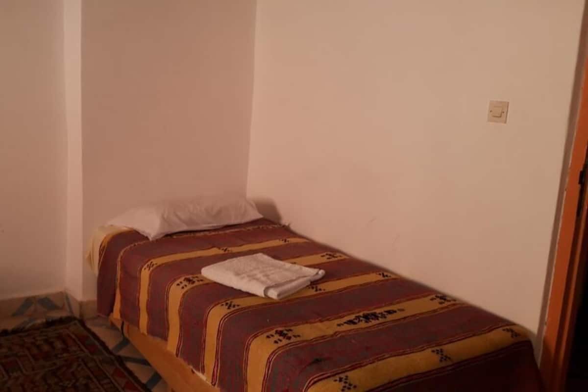 Une petite chambre avec un lit simple, une couvre-lit à motifs et un oreiller blanc.