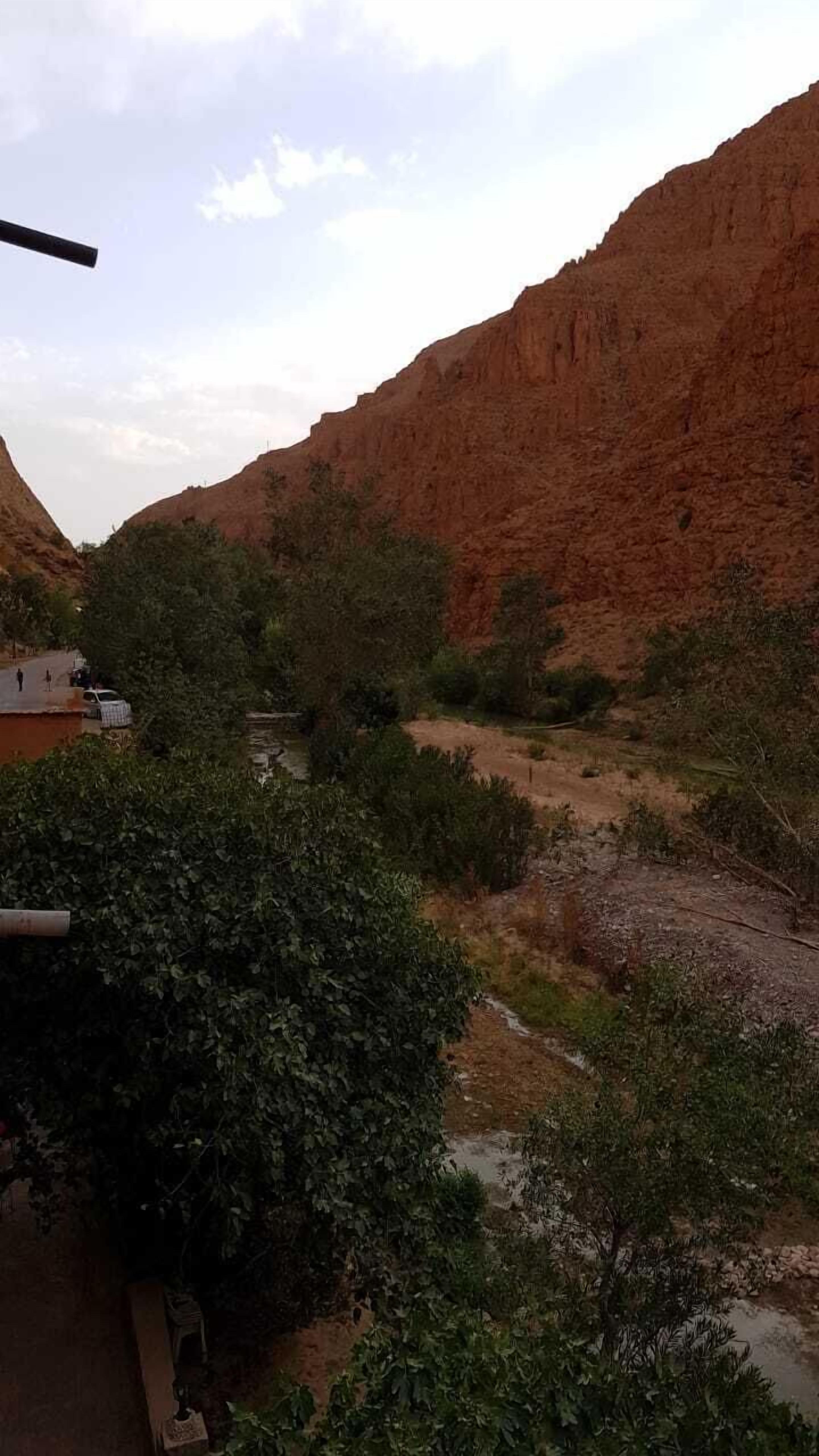 A mountainous landscape with a river, vegetation, and a building in the foreground.