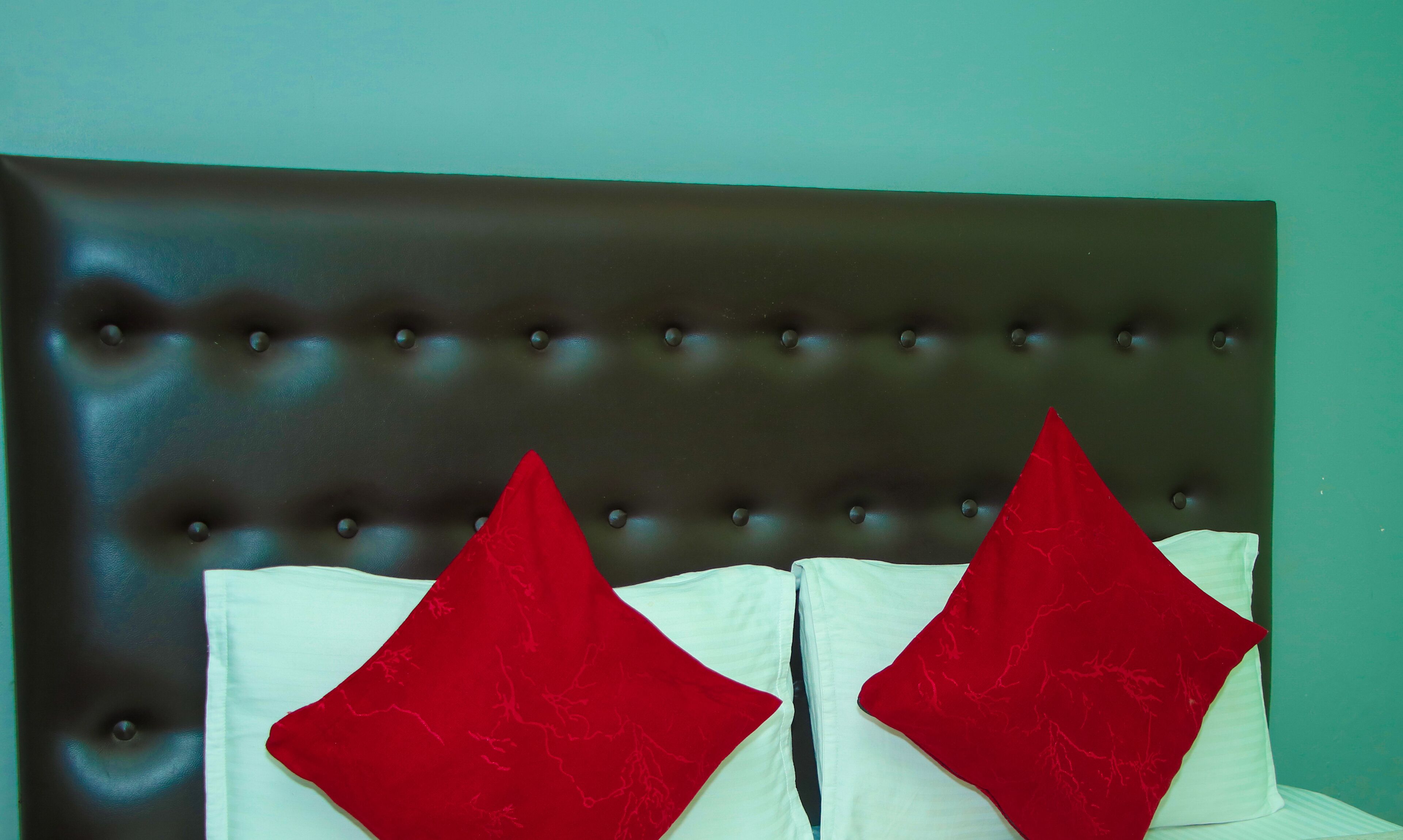 Una cama con cabecera capitonada y dos almohadas rojas.