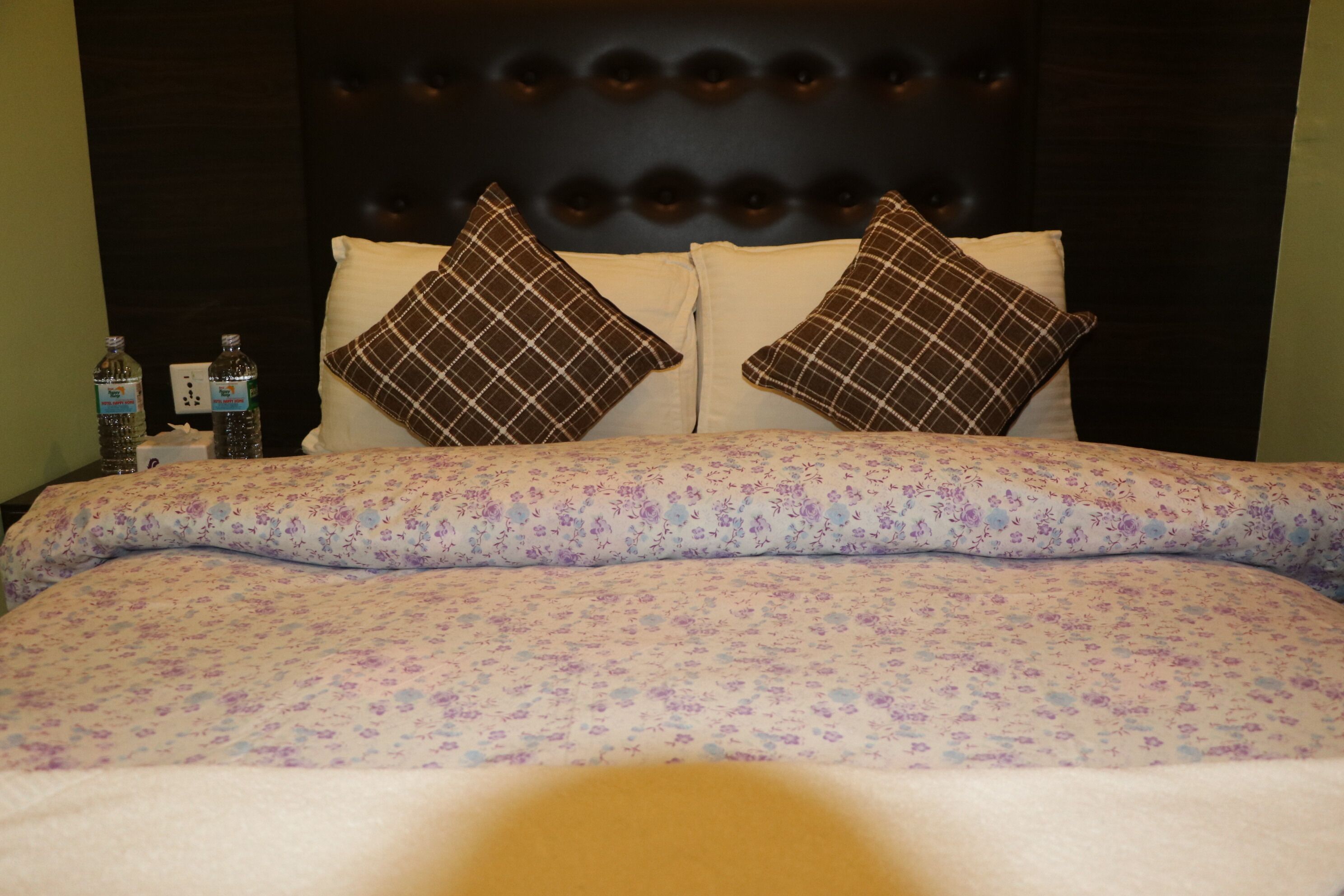 Una cama con ropa de cama floral, dos almohadas a cuadros y un cabecero oscuro.