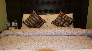 Una cama con ropa de cama floral, dos almohadas a cuadros y un cabecero oscuro.