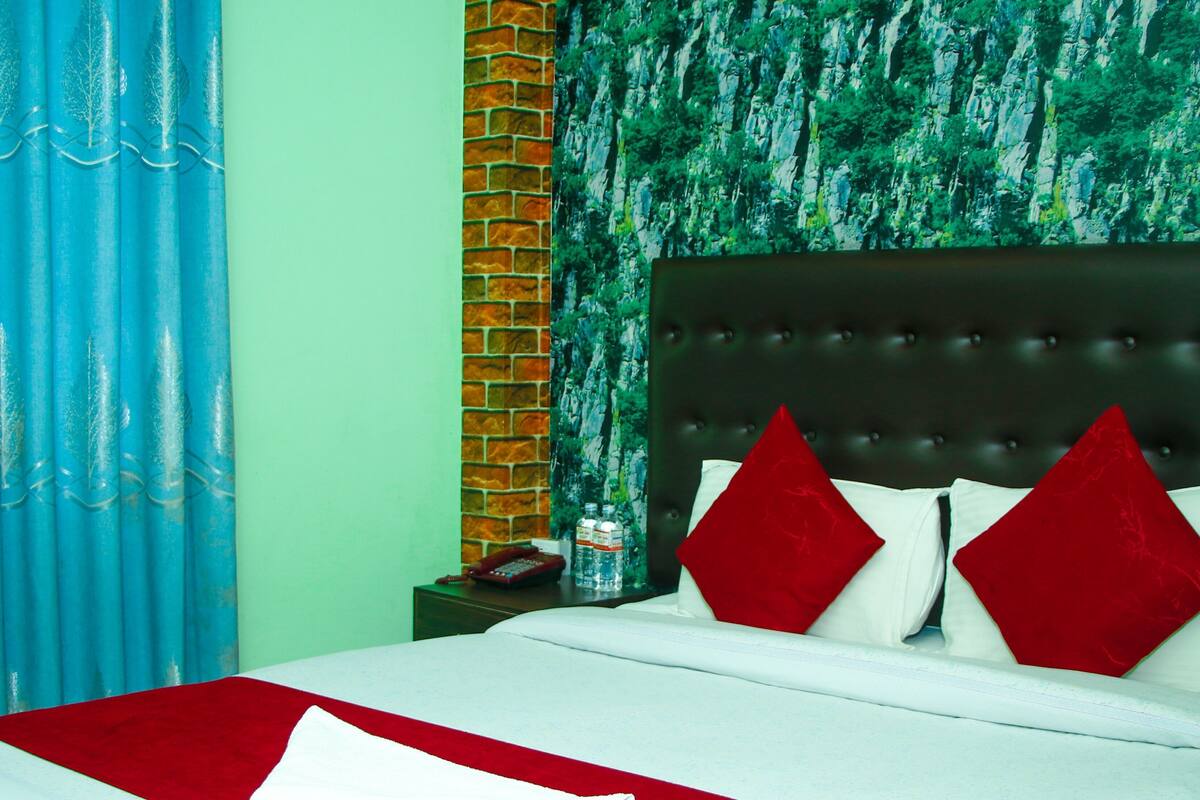 Habitación de hotel con cama, almohadas, mesita de noche, control remoto y una botella de agua.
