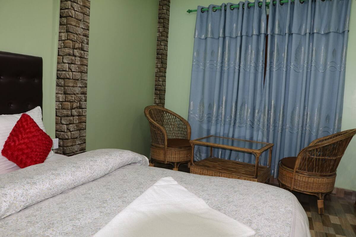 Un dormitorio con una cama, dos sillas de mimbre, una mesita de madera y una cortina azul.
