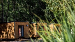 A row of wooden cabins with a dirt ground, surrounded by dense forest. - Les Voiles de Laives (Laives)