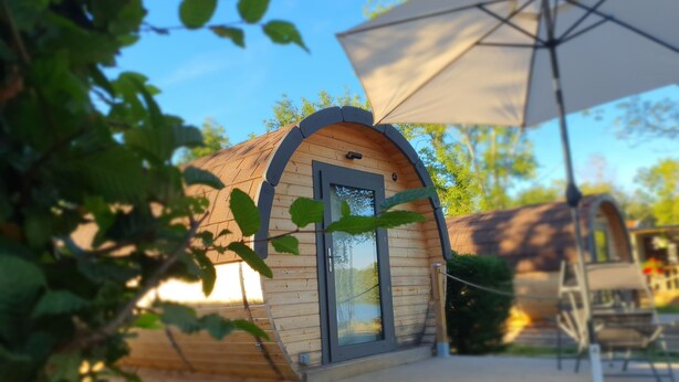A wooden cabin with a large window, a door, and a covered patio area with a table and chairs. - Les Voiles de Laives (Laives)