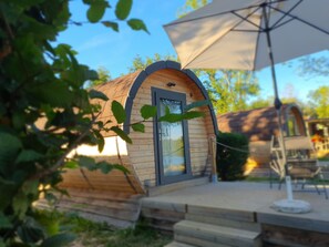 Una cabaña de madera con un ventanal grande, una puerta y un porche cubierto con una mesa y sillas.