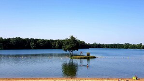 A lake with a sandy beach, a small island with a tree, and a clear blue sky. - Les Voiles de Laives (Laives)