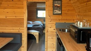 A cozy wooden cabin interior with a kitchenette, a bed with a view, and a dining area. - Les Voiles de Laives (Laives)