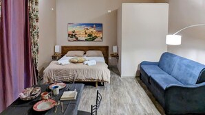 Una habitación de hotel con cama, una mesa de comedor con sillas, un sofá y un cuadro en la pared.