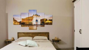 Un dormitorio con una cama grande, un cabecero de madera, dos mesitas de noche con lámparas y una obra de arte en la pared que muestra un edificio.