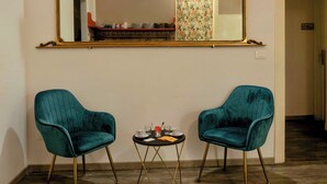 Una habitación con dos sillas color turquesa, una pequeña mesa redonda con una taza y un platillo, y un espejo grande y decorativo en la pared.