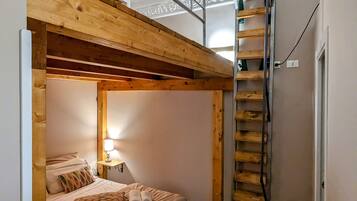 Una habitación con una cama litera, una escalera, una mesita de noche con lámpara y un ventanal pequeño.