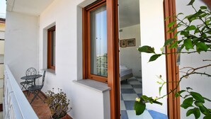 Un balcón con mesa y sillas, una planta en maceta y vistas del interior a través de una puerta de cristal.