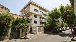 Un edificio residencial de varios pisos con balcones, una entrada porticada y coches aparcados a lo largo de la calle.