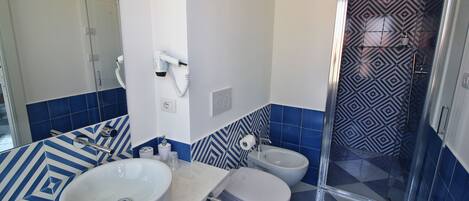 Un baño con un lavamanos blanco, dos inodoros, una ducha y un salpicadero de azulejos con diseño.