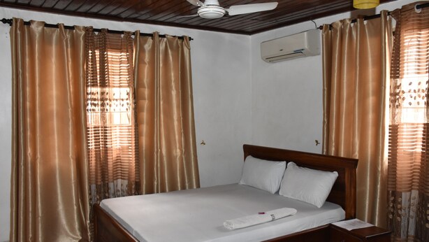 A neatly made bed with white linens, a wooden headboard, and a nightstand with a lamp. - Dar eco backpackers (Dar es Salaam)