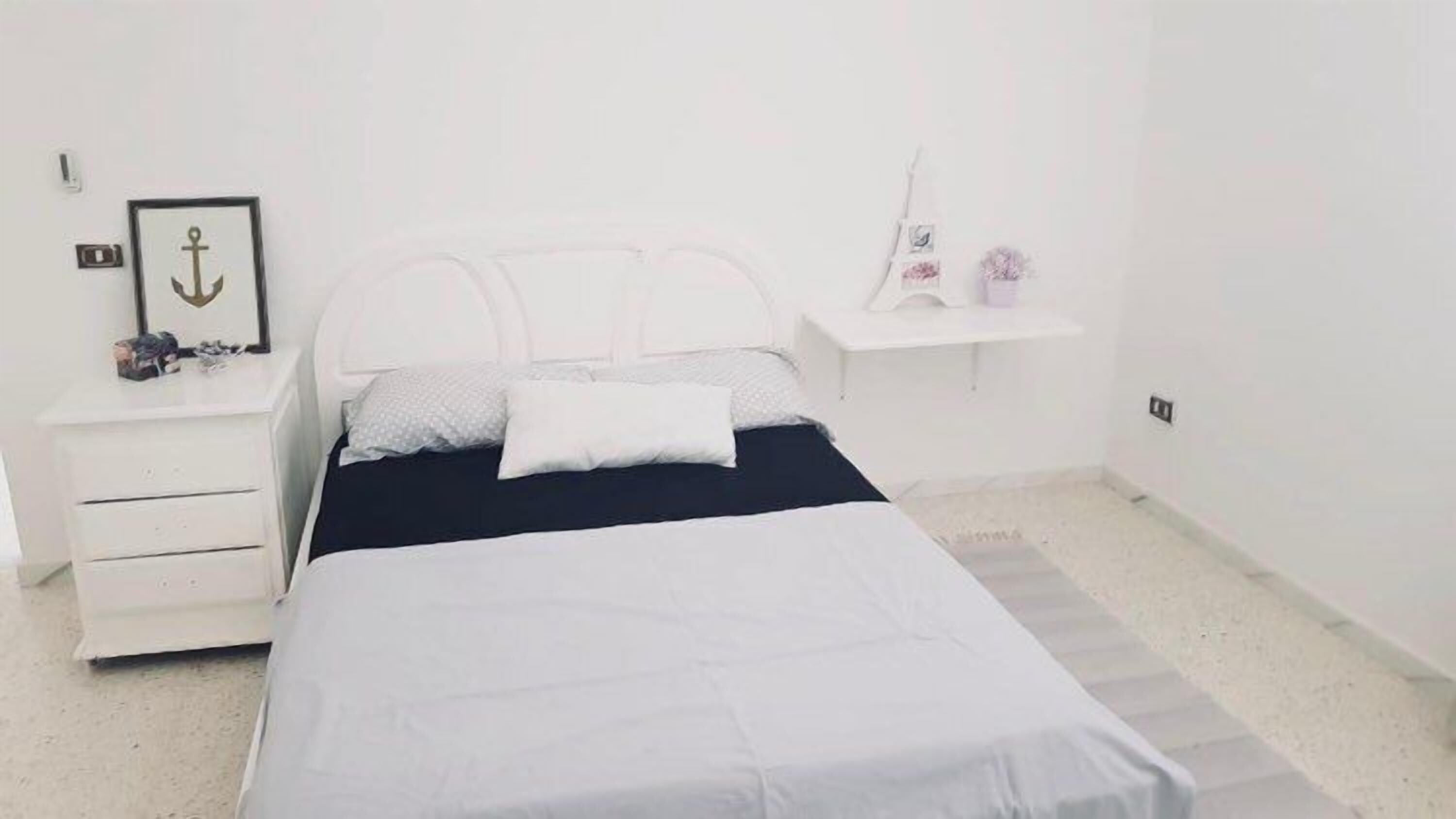 A minimalist bedroom with a bed, a nightstand, and a small shelf.