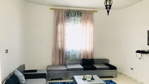 Una sala de estar con sofá, dos camas, una mesita de centro y un tapete estampado.