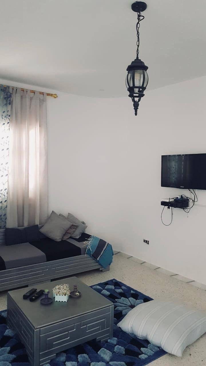 Una sala de estar moderna con un sofá, una mesa de centro, un televisor de pantalla plana montado en la pared y una lámpara colgante.