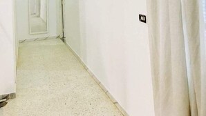 Un pasillo con paredes blancas y piso de baldosas, que conduce a una puerta al final.