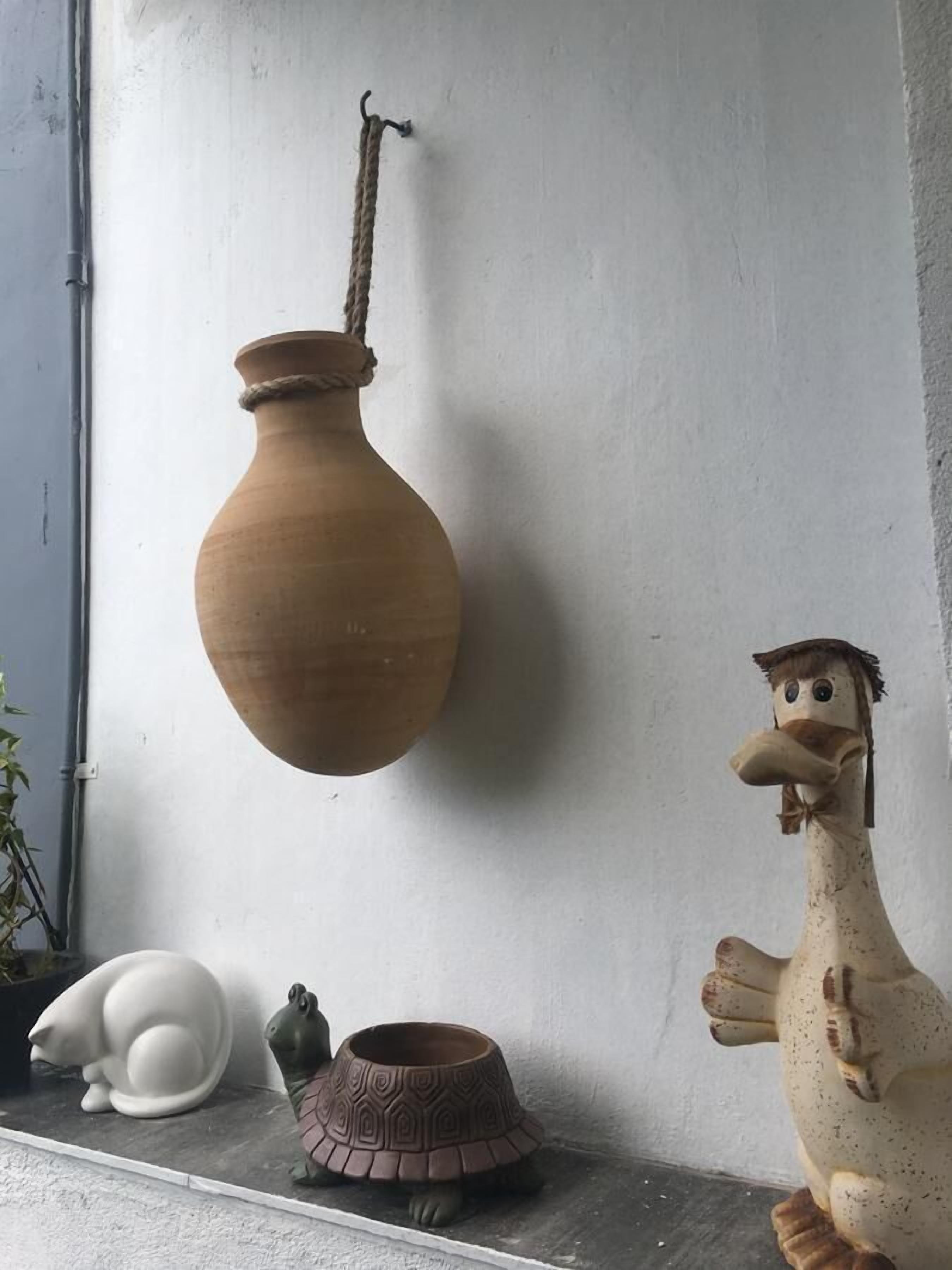 A rustic interior with a hanging clay pot, a ceramic frog, a ceramic turtle, and a ceramic rooster.