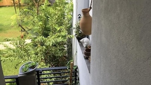 Ein Balkon mit Blumentöpfen, einem hängenden Laternen und Blick auf einen Garten.