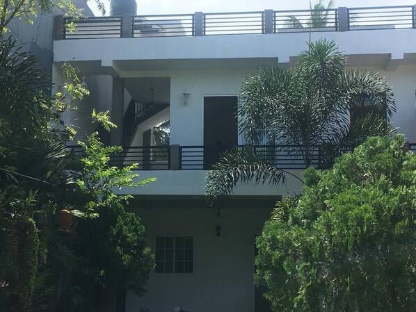 Un immeuble de deux étages doté d’un balcon à l’étage supérieur, entouré de verdure.