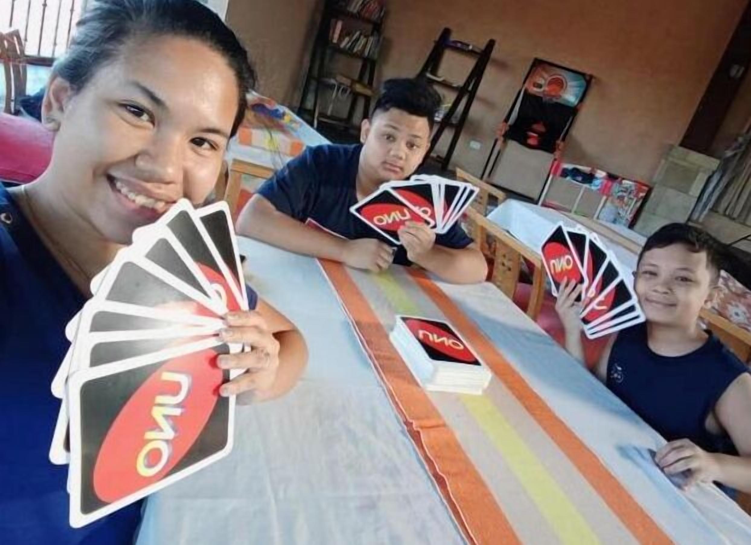 Un groupe de personnes est assis autour d’une table recouverte d’une nappe à rayures et tient des cartes à jouer.