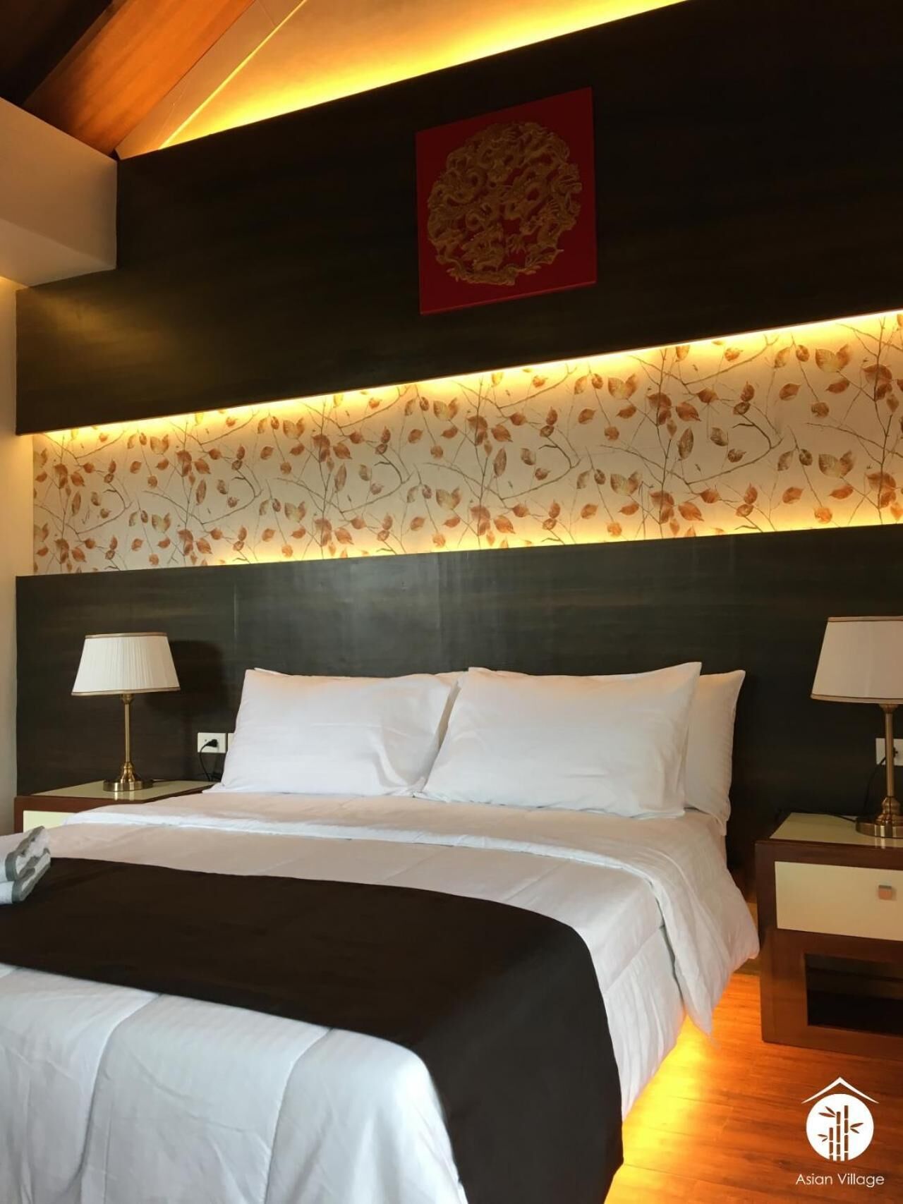 Una habitación de hotel moderna con una cama grande, dos mesitas de noche con lámparas, un panel decorativo en la pared y una obra de arte roja sobre la cama.