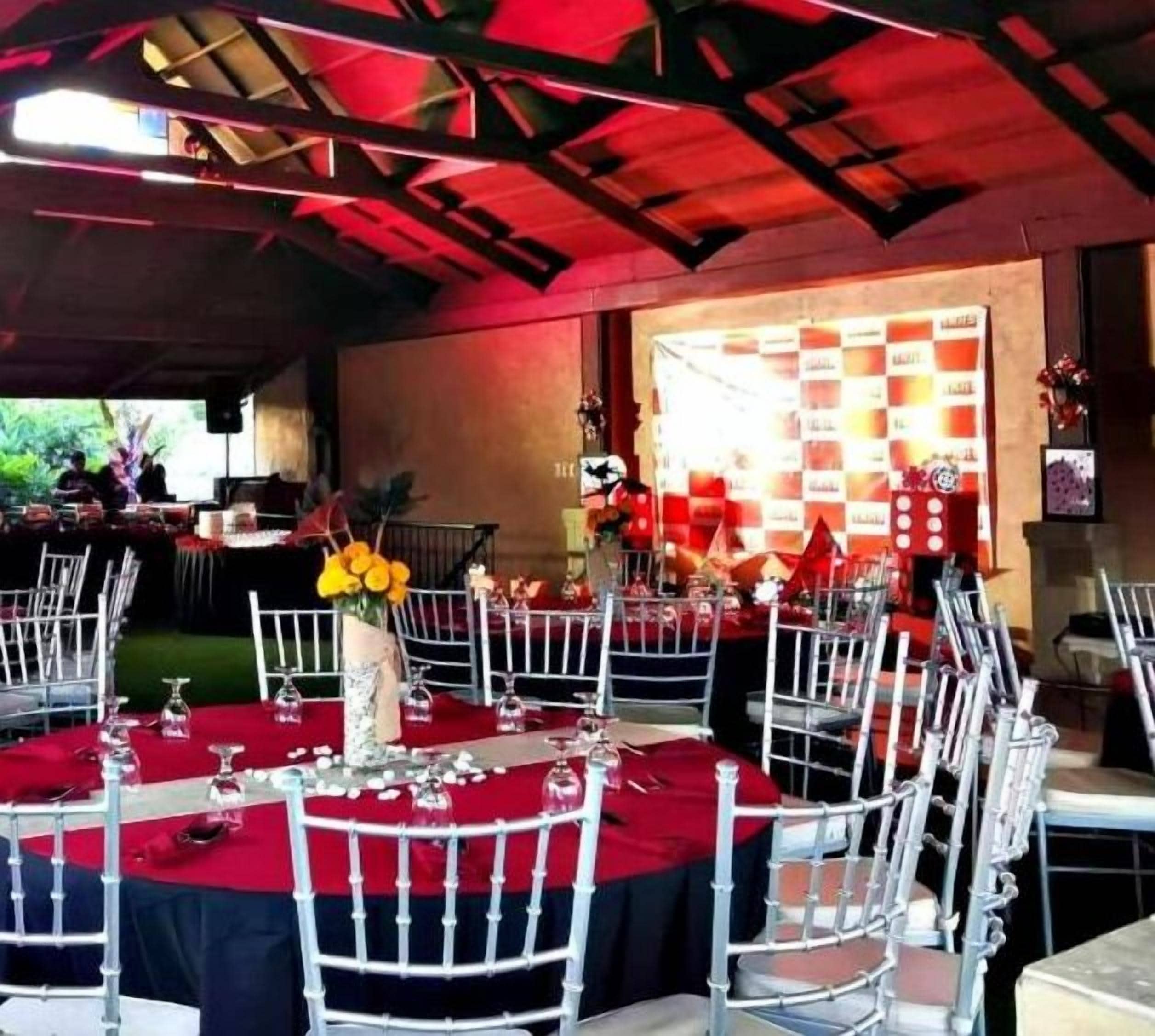 Un salón de banquetes con mesas redondas cubiertas con manteles rojos, sillas blancas y cristalería.