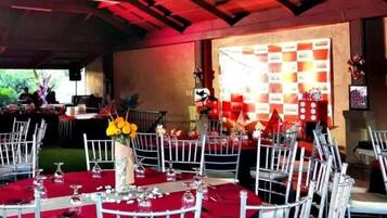 Un salón de banquetes con mesas redondas cubiertas con manteles rojos, sillas blancas y cristalería.