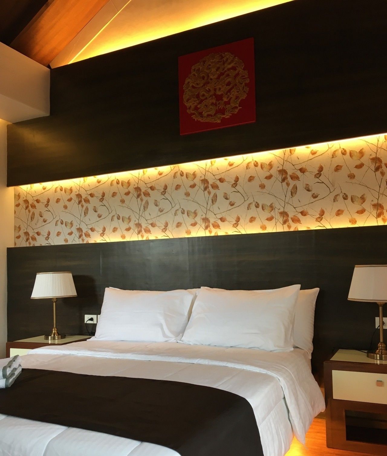 A hotel room with a large bed, two bedside tables with lamps, a decorative wall panel, and a red artwork above the bed.