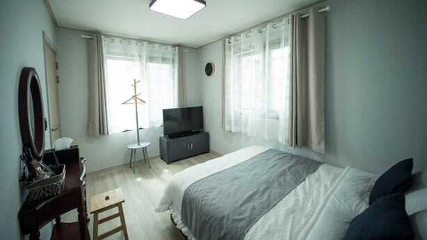 A bedroom with a bed, a TV, a dresser, a mirror, and a window with curtains.