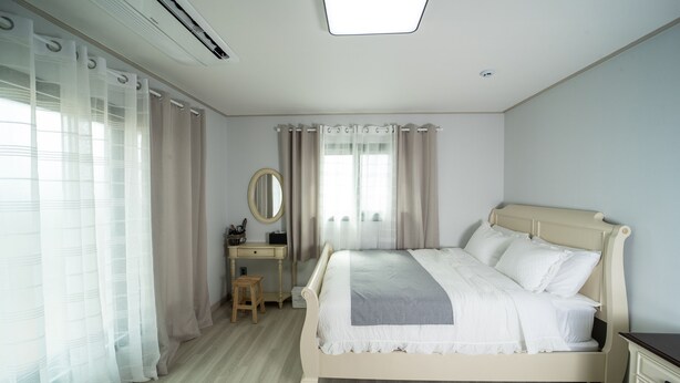 A bedroom with a bed, a nightstand, a dresser, a mirror, and a window with curtains. - rabbit foot renthouse (Jeju City)